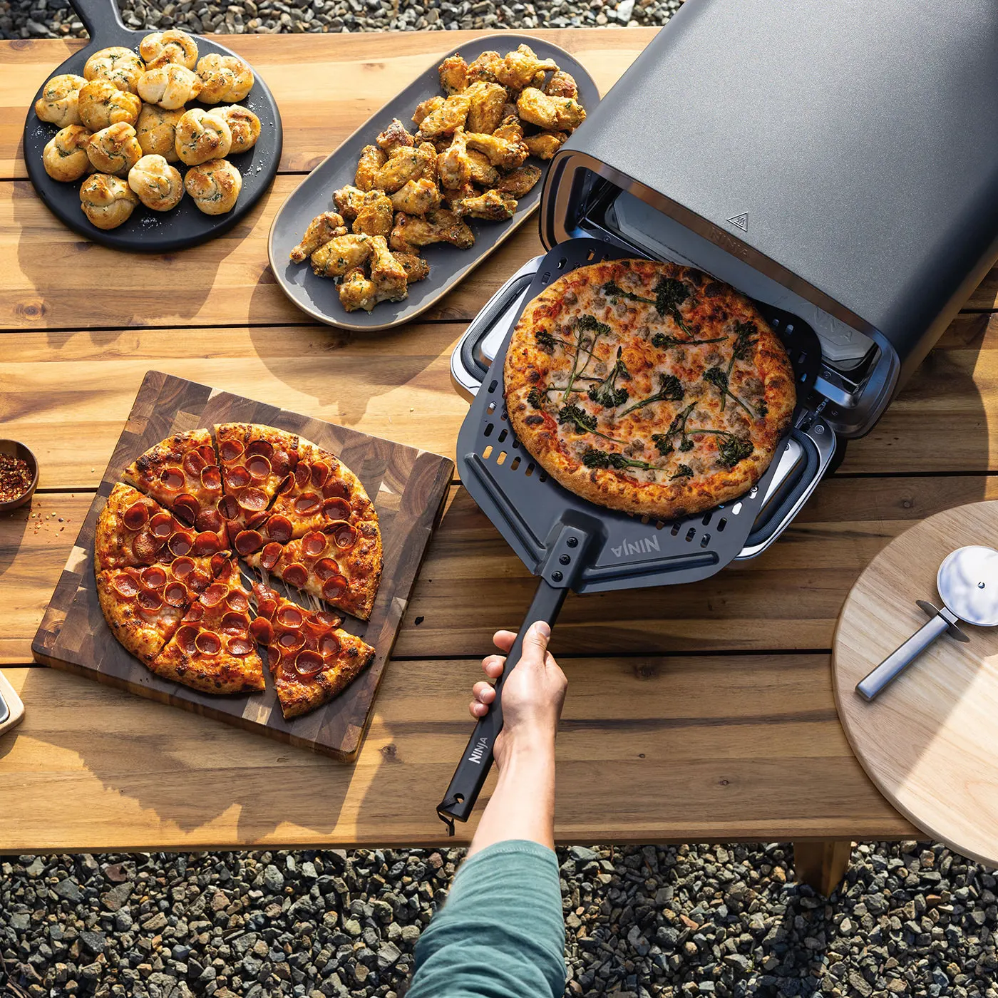 Ninja-MO201UK-InUse-BackYard-OnTable-Wings-Desert-Casserole-RemovingPizza-Man